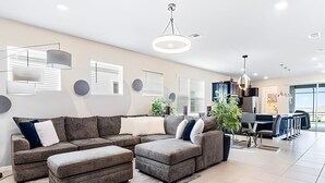 En moderne stue med en hjørnesofa, skammel og et spiseområde med bar.