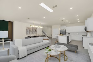 Un salon moderne avec un canapé blanc, une table basse et un escalier menant à la cuisine.