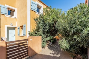Un estrecho callejón con un edificio amarillo, una puerta de madera y abundante vegetación.