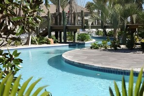 En pool med buet kant, omgivet af palmer og anden vegetation.