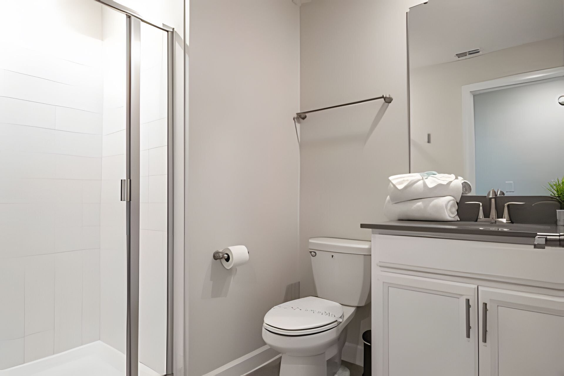 Ein modernes Badezimmer mit Duschkabine aus Glas, Toilette und Waschbecken mit Handtuchhalter.