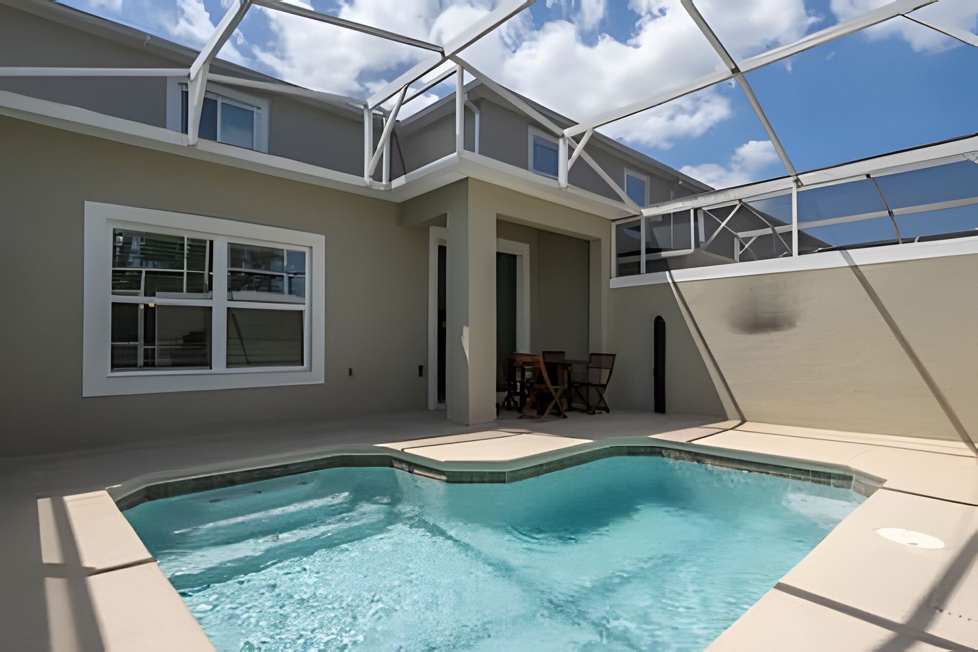 A swimming pool area with a covered patio, a door leading to an interior space, and a clear blue sky.