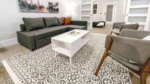 Uma sala de estar moderna com um sofá seccional, uma mesa de centro branca, tapete estampado e poltronas cinzas.