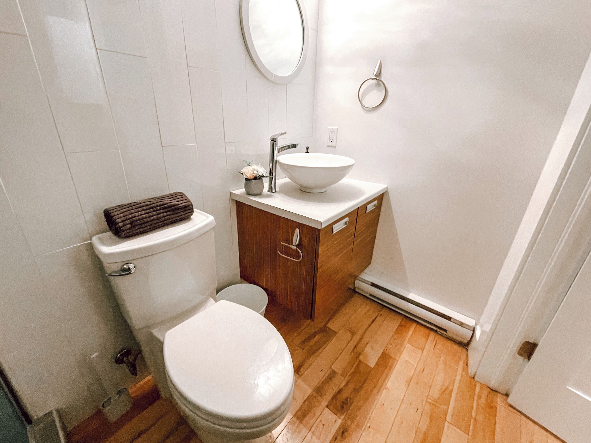 Un baño pequeño y moderno con un inodoro blanco, un tocador de madera con lavabo y un espejo sobre el tocador.