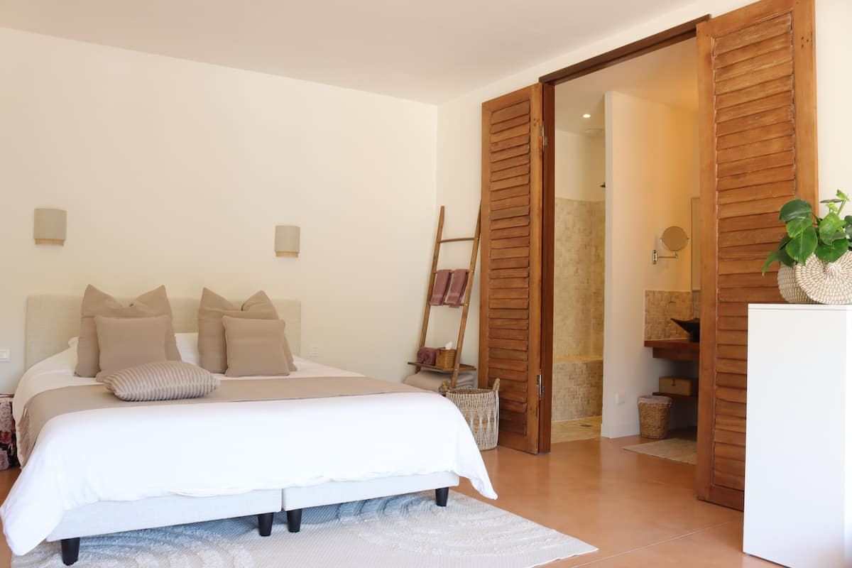 Un dormitorio con cama, contraventanas de madera, una planta y una cesta pequeña.