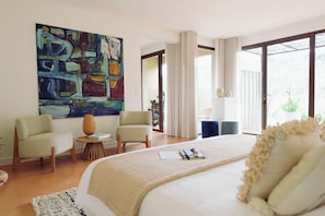 A modern hotel room with a large bed, two armchairs, a small table, and a large abstract painting on the wall. - Louis Henry (Saint-Pierre-des-Champs)