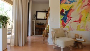 A living room with a chair, a table, a painting, and a large window with curtains. - Louis Henry (Saint-Pierre-des-Champs)