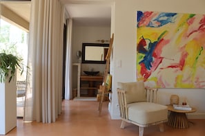 Ein Wohnzimmer mit einem Sessel, einem Tisch, einem Gemälde und einem großen Fenster mit Vorhängen.