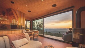 A modern living room with a large window, wooden ceiling, and a cozy seating area.