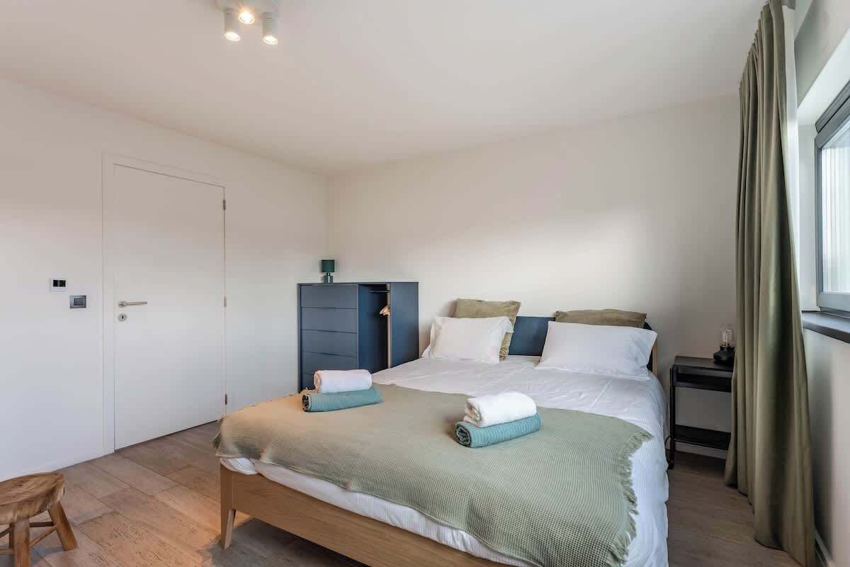 Een slaapkamer met een bed, nachtkastje, kledingkast en een raam met gordijnen.