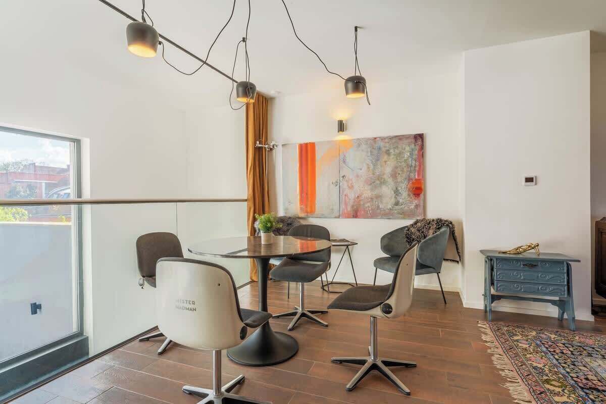 Una sala de estar moderna con comedor, que presenta un ventanal grande, una obra de arte contemporánea y una mesita auxiliar azul.