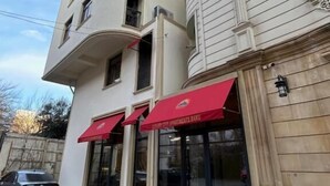 Ein mehrstöckiges Gebäude mit moderner Fassade, das große Glasfenster und ein rotes Markisenwerbeschild mit dem Text "Luxury City Apartments Baku" zeigt.
