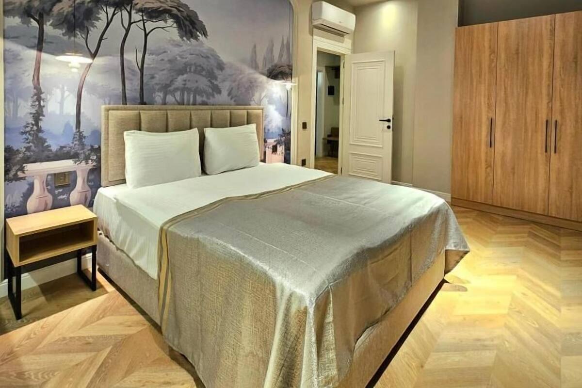 Een slaapkamer met een groot bed, een nachtkastje, een kledingkast en een muurschildering.