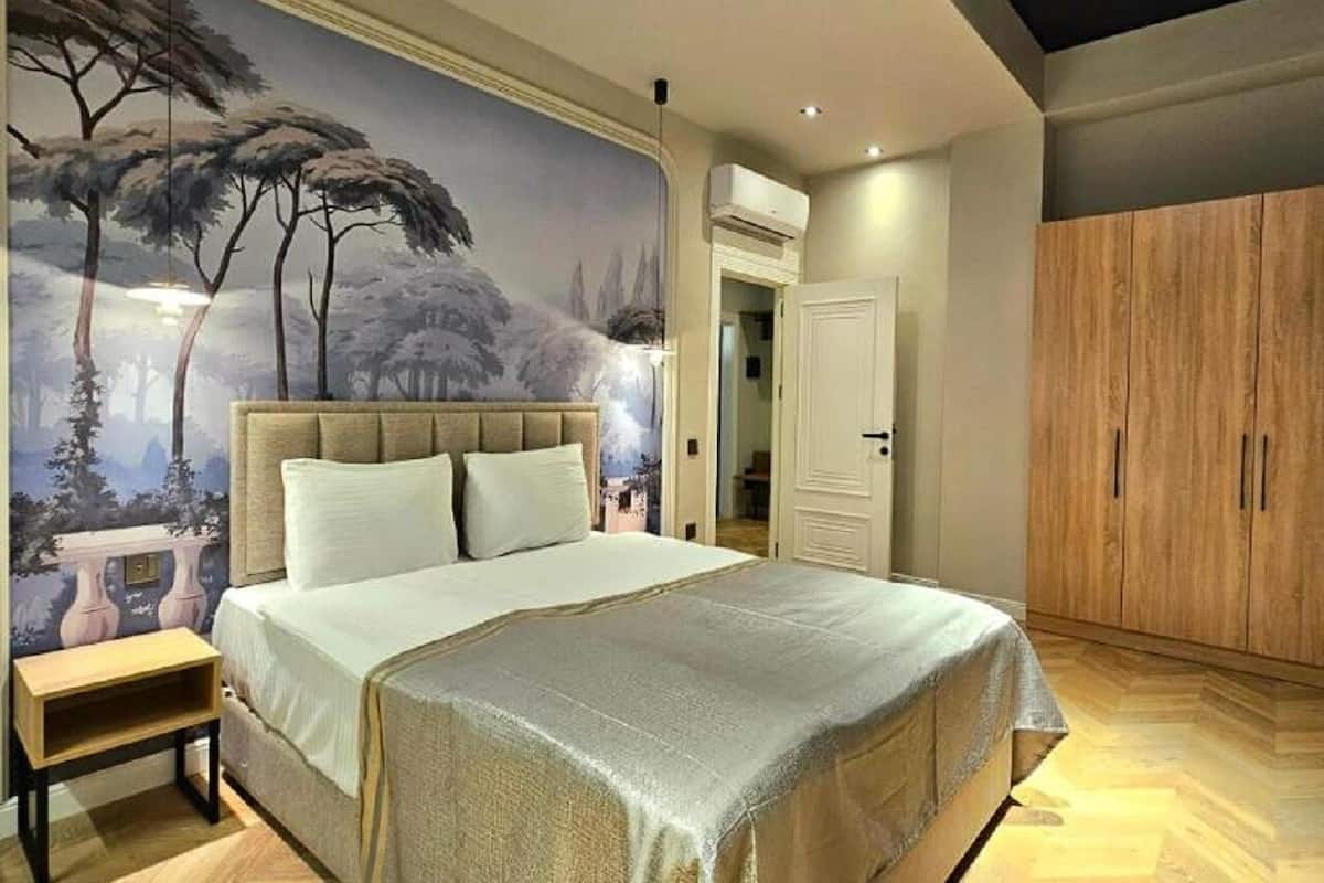 Een slaapkamer met een groot bed, een nachtkastje, een garderobe en een muurschildering.
