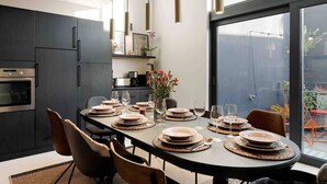 Une cuisine moderne avec des meubles de couleur sombre, un four encastré et un coin repas doté d’une table ronde prévue pour accueillir six personnes.
