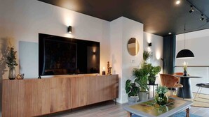 Un espace d’accueil moderne avec un comptoir de réception en bois, un grand téléviseur à écran plat, des plantes en pot et un grand miroir rond accroché au mur.