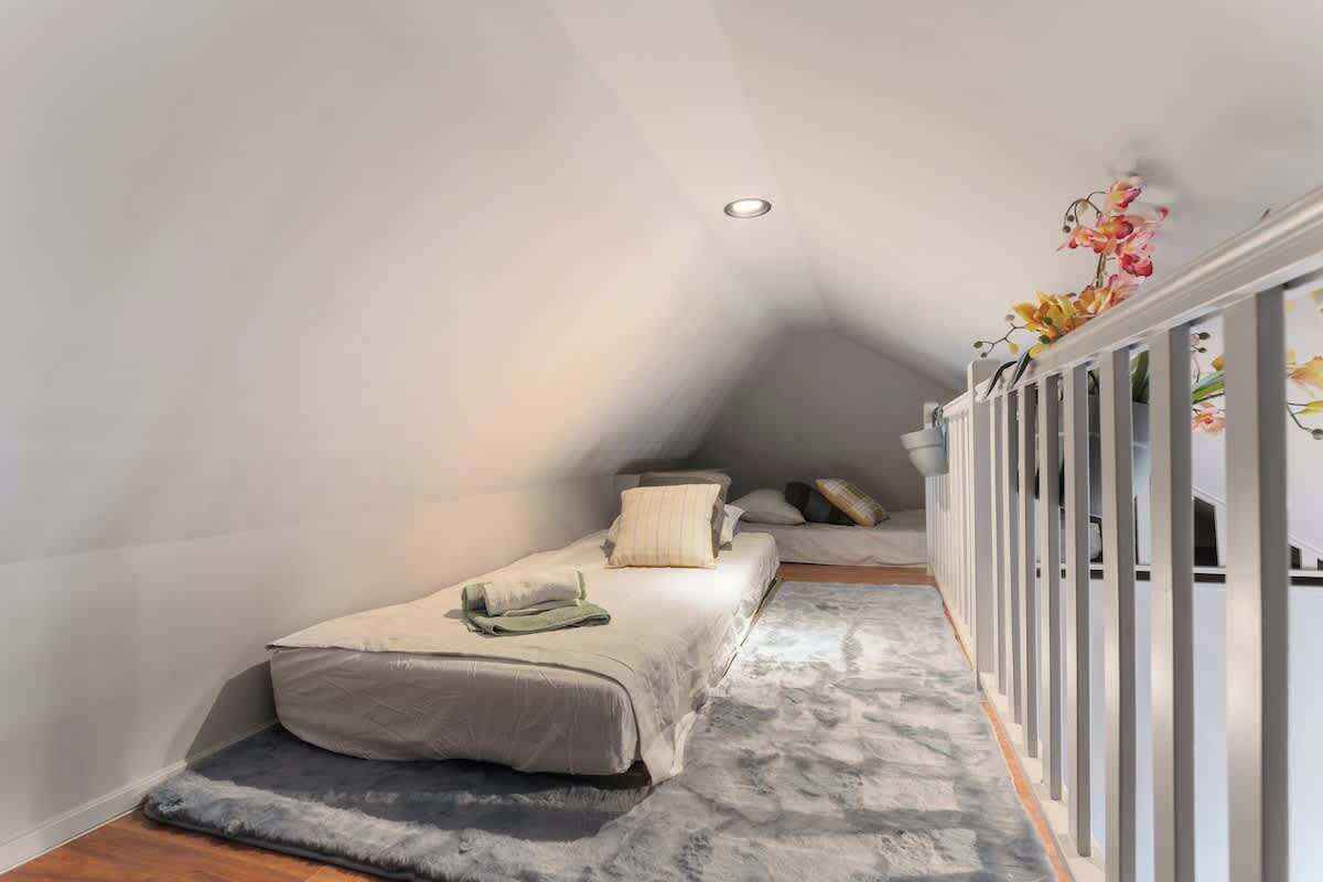 A narrow, sloped bedroom with a bed, pillows, and a small rug.