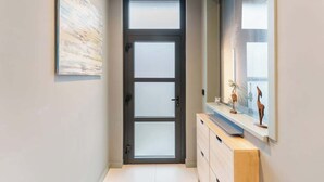 A hallway with a modern door, a light-colored wall, and a wooden cabinet with decorative items. - Elegant & Spacious House close to Center (Kortrijk)
