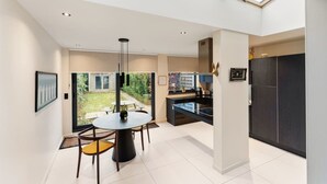 A modern kitchen with a large island, a dining area with a round table and chairs, and a view of a garden through large windows. - Elegant & Spacious House close to Center (Kortrijk)