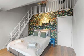 Une chambre à coucher comprenant un lit, une table de chevet, une commode, un escalier et un papier peint à motifs floraux.