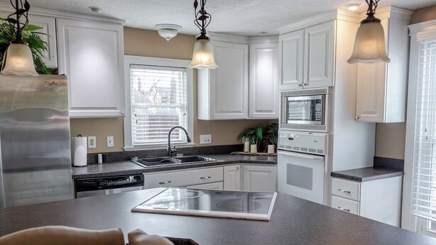 Una cocina moderna con armarios blancos, un refrigerador de acero inoxidable, un microondas y un horno empotrado.