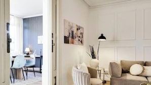 Een moderne woonkamer met een bank, fauteuil en een eethoek op de achtergrond.