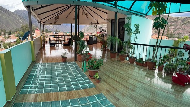A covered outdoor area with a wooden floor, potted plants, and a view of mountains. - hotel killa (Urubamba)