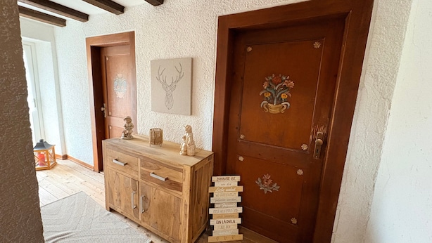 A wooden cabinet with drawers, a door with a floral design, and a wall-mounted deer head artwork. - Apartment 'Landliebe' with Mountain View, Shared Terrace, and Wi-Fi (Münstertal)