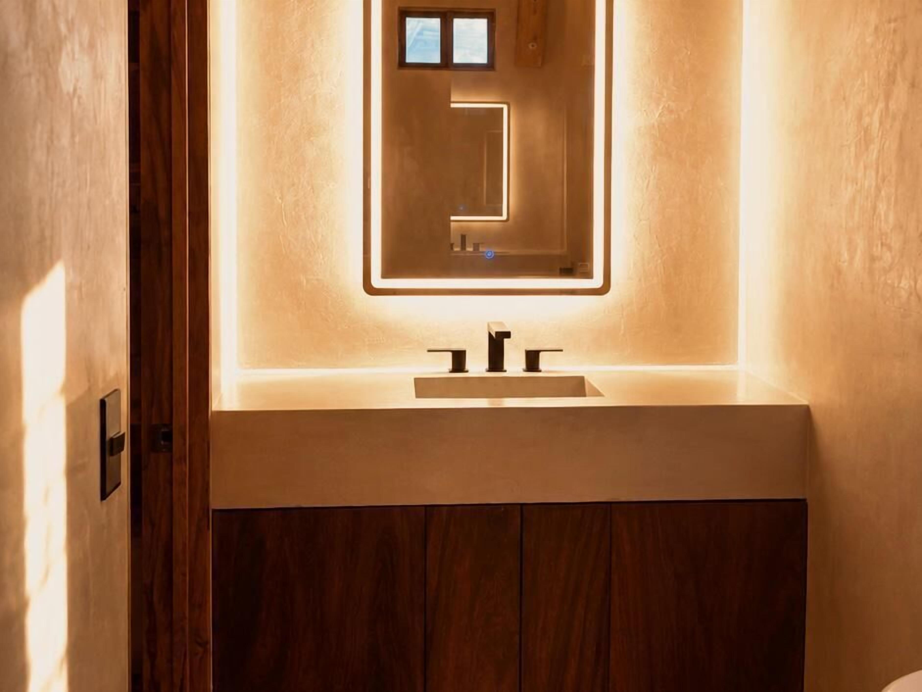A bathroom with a wooden vanity, a mirror with integrated lighting, and a modern faucet.