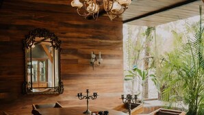 A rustic dining area with a long wooden table, chairs, a chandelier, a mirror, and a view of greenery outside. - Casona Tunan (Mizata)