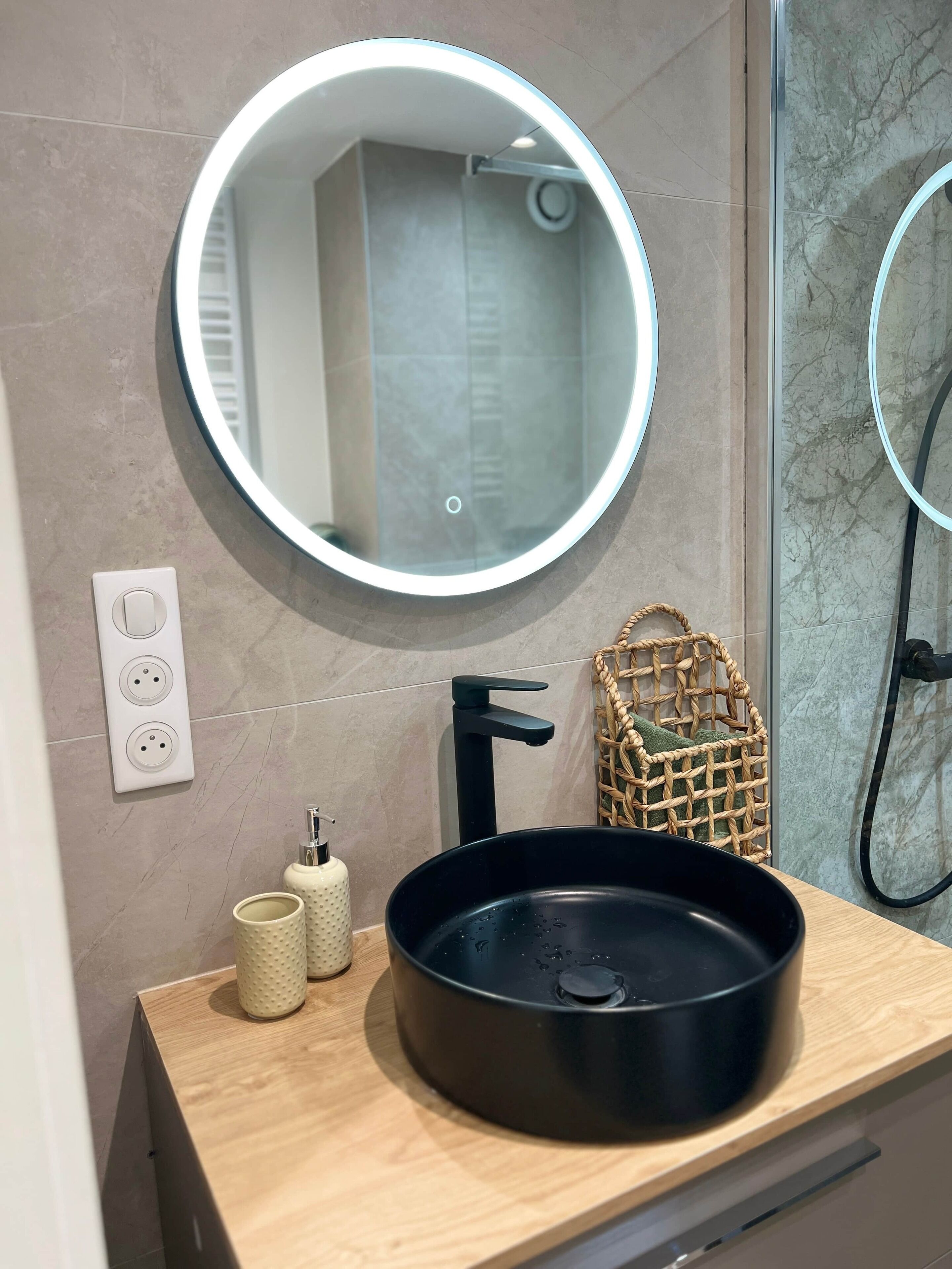 A bathroom with a round mirror, a black sink, a towel rack, and a wicker basket.