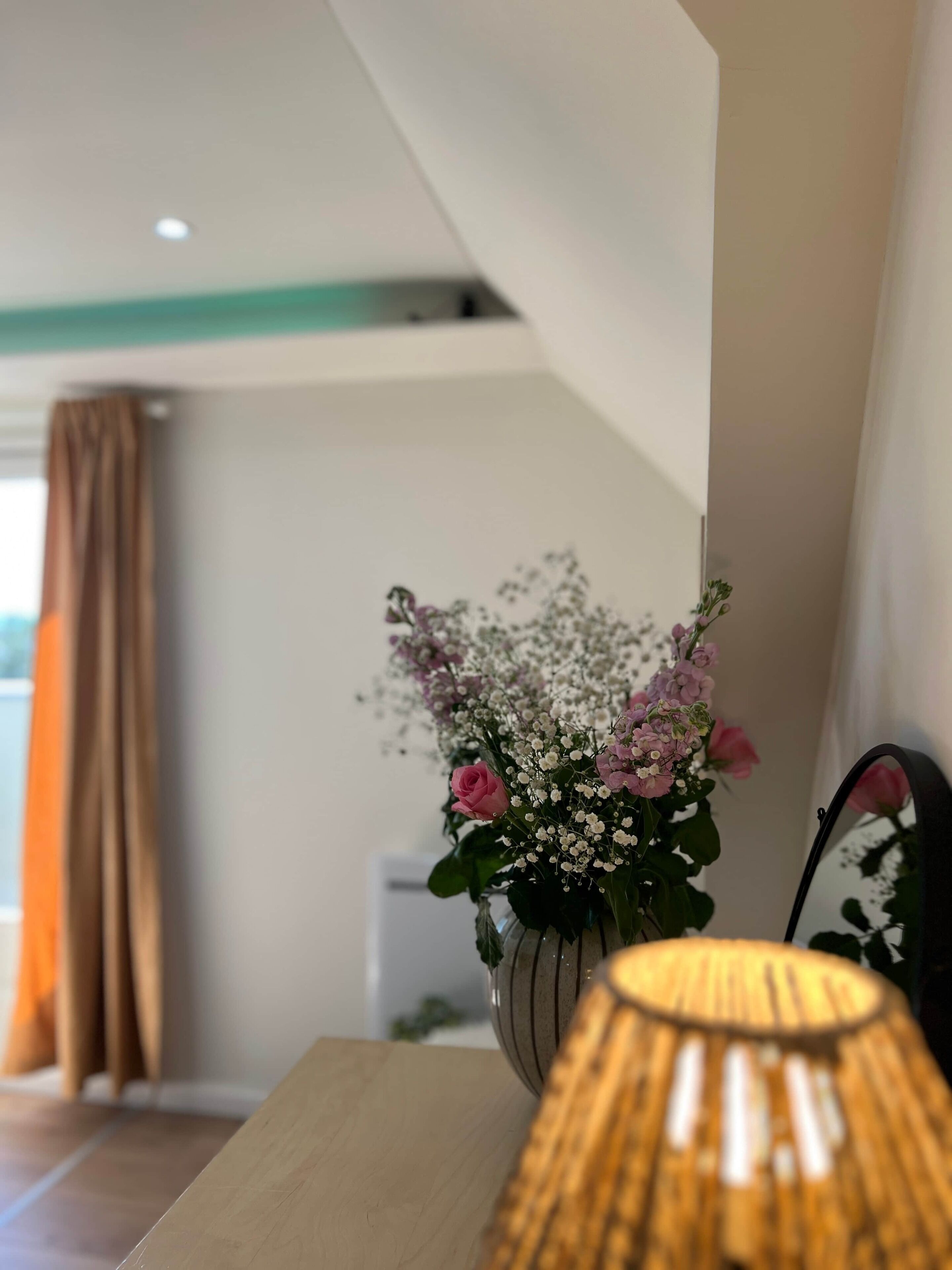 Et værelse med et træbord, en vase med blomster og en lampe.