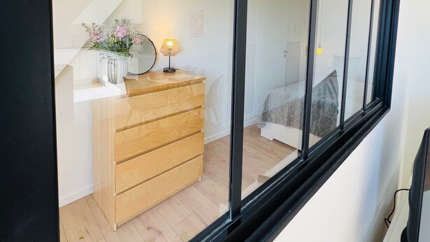 Ein modernes Schlafzimmer mit einem Holzkleiderschrank, einem Nachttisch mit Lampe und einem Bett mit gemustertem Bettbezug.