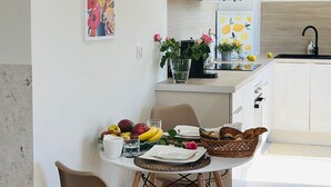 Eine moderne Küche mit weißen Schränken, einem Essbereich mit Tisch für zwei Personen und einer Kücheninsel mit Spüle und Obstschale.