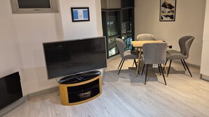 Uma sala de estar moderna com televisão de tela plana, uma mesa de jantar com cadeiras e uma janela grande com vista para a cidade.