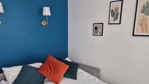Quarto de hotel com cama, parede azul decorativa, luminária fixada na parede e obras de arte emolduradas.