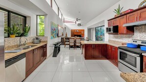 A modern kitchen with granite countertops, wooden cabinets, a built-in oven, and a dining area with a sofa and chairs. - Casa Lumina – Contemporary 3-Bedroom Villa with Private Pool - 6 Guests (Playas del Coco)