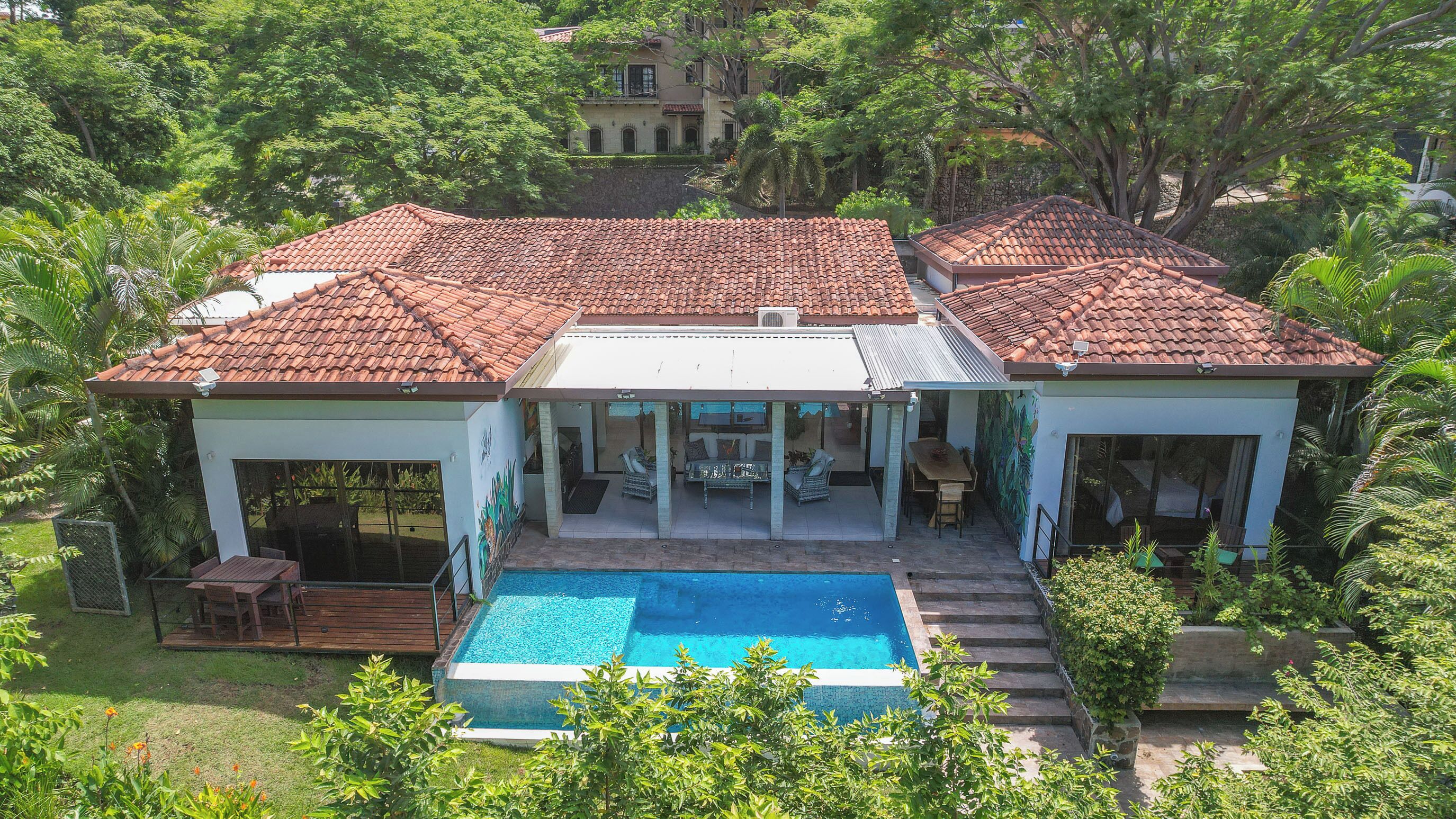 Une maison à deux étages dotée d’une piscine, d’un patio couvert et d’une végétation luxuriante.
