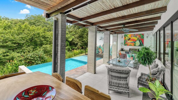 A poolside area with a glass table and wicker chairs, surrounded by lush greenery and a large mural. - Casa Lumina – Contemporary 3-Bedroom Villa with Private Pool - 6 Guests (Playas del Coco)
