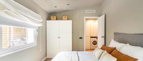 Ein Schlafzimmer mit Bett, Kleiderschrank, Waschmaschine und einem Fenster mit Jalousien.