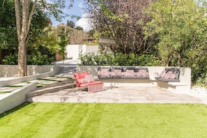 A landscaped outdoor area with a seating arrangement, a pathway, and a view of a building in the background. - Villa Atardecer—15' from Barcelona / BBQ / Pool (CT)