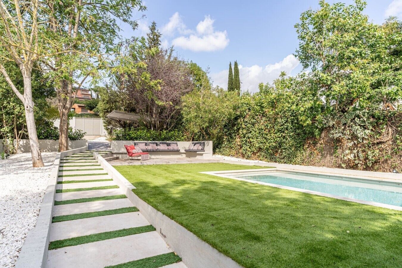 Un patio trasero con piscina, césped y un espacio de estar con mobiliario exterior.