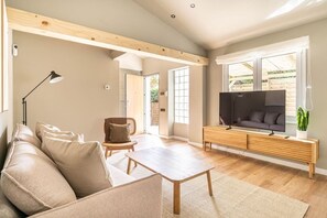 A modern living room with a sofa, a coffee table, a TV on a wooden stand, and a plant. - Villa Atardecer—15' from Barcelona / BBQ / Pool (CT)
