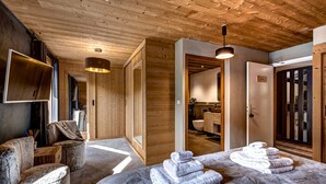Interno di una baita in legno con un letto, una TV e un bagno visibile attraverso una porta aperta.