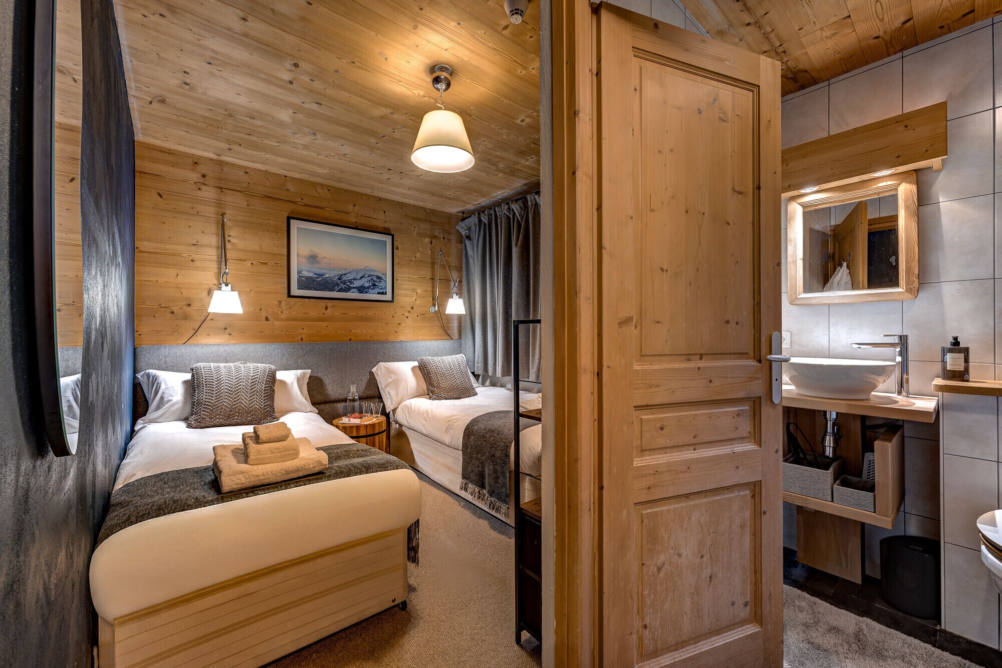 Hotellihuone, jossa on puinen katto, suuri sänky tyynyineen, yöpöytä ja näkymä vuorille.