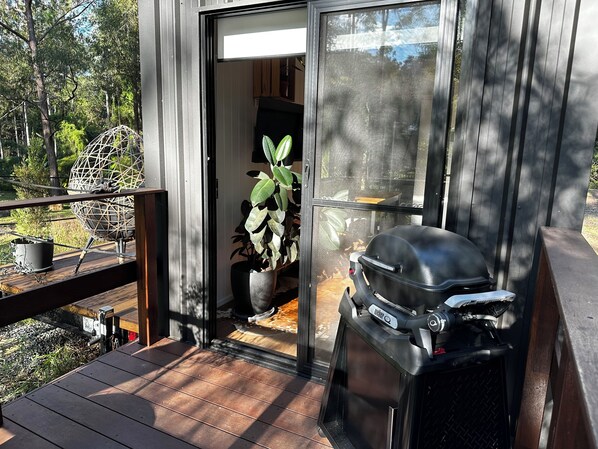 A modern outdoor deck with a grill and potted plants. - Luxury Tiny House Retreat | Private Chef Dining (Pie Creek)
