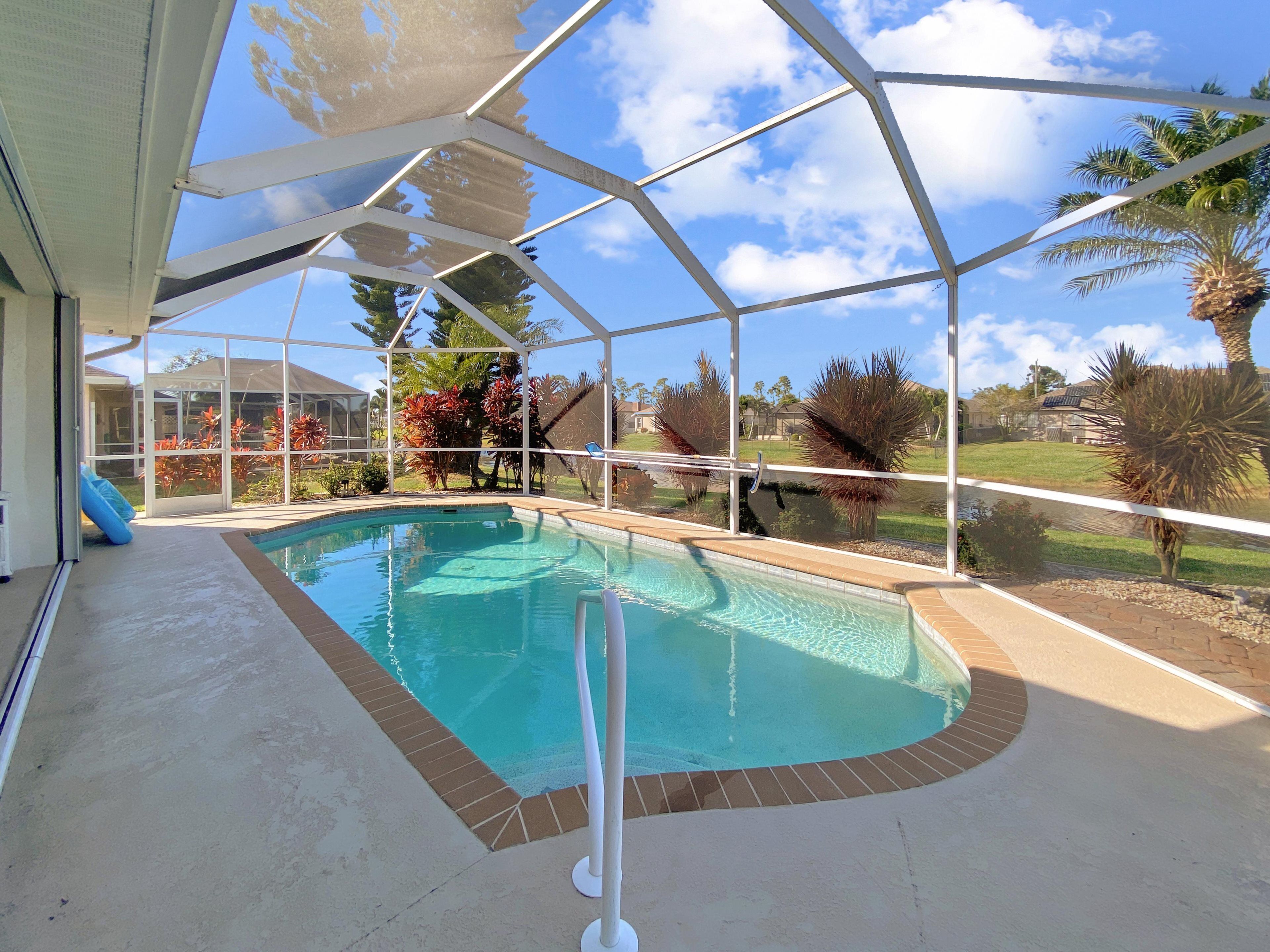 Una piscina cubierta con vistas despejadas del paisaje circundante, incluyendo palmeras y una casa al fondo.