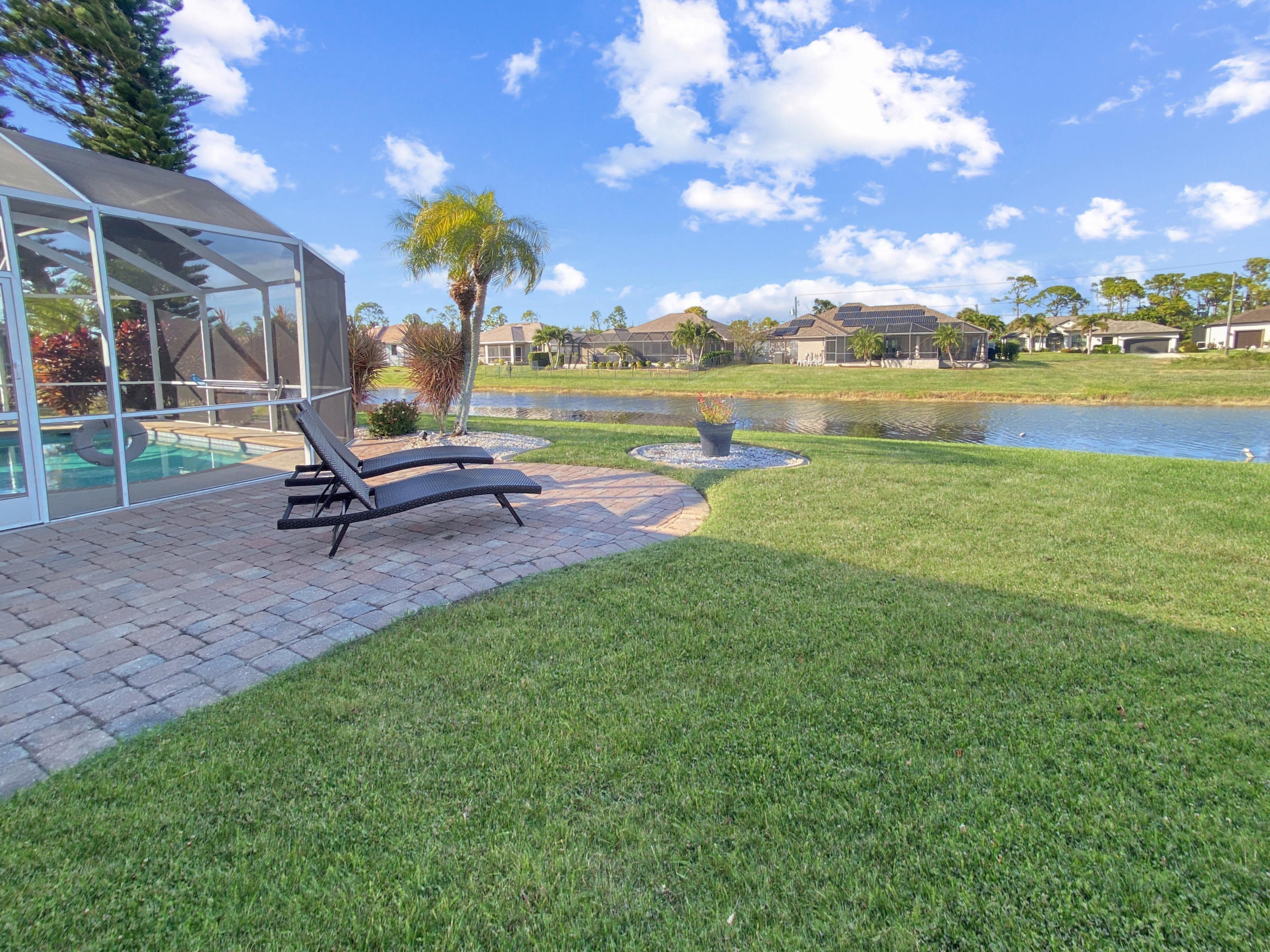 A poolside area with lounge chairs, a covered patio, and a view of a lake and houses in the background.