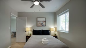 Ein Schlafzimmer mit einem Bett, zwei Nachttischlampen, einem Deckenventilator, einem Fenster mit Jalousien und einem Bild an der Wand.