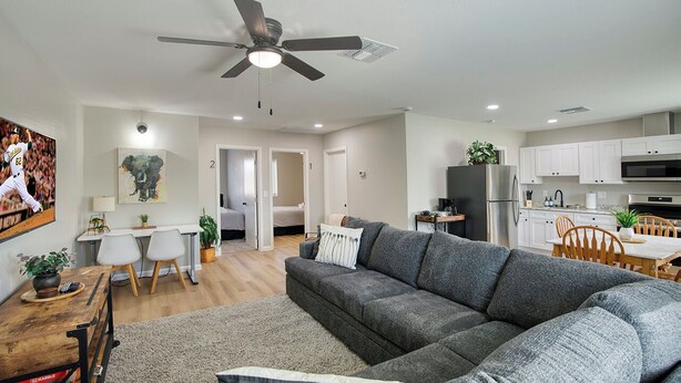 Ein modernes Wohnzimmer mit einem grauen Sofa, einem Holztisch und einem Deckenventilator.